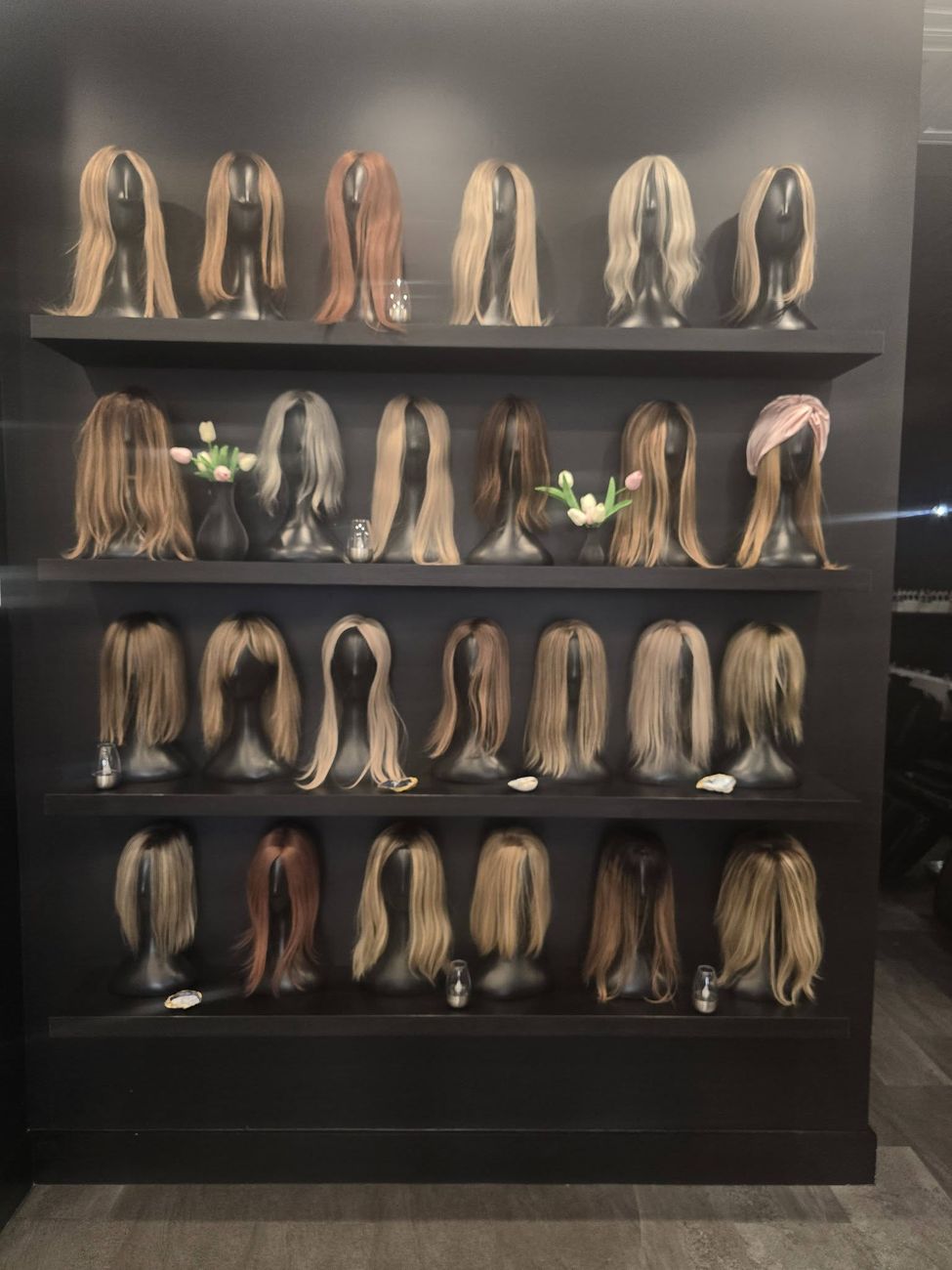 Wall of custom hair toppers and wiglets color-matched in the Salon East Naples fitting studio