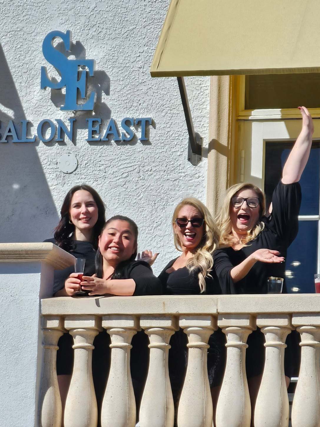 The Salon East team on the balcony beneath the salon sign on 5th Avenue South